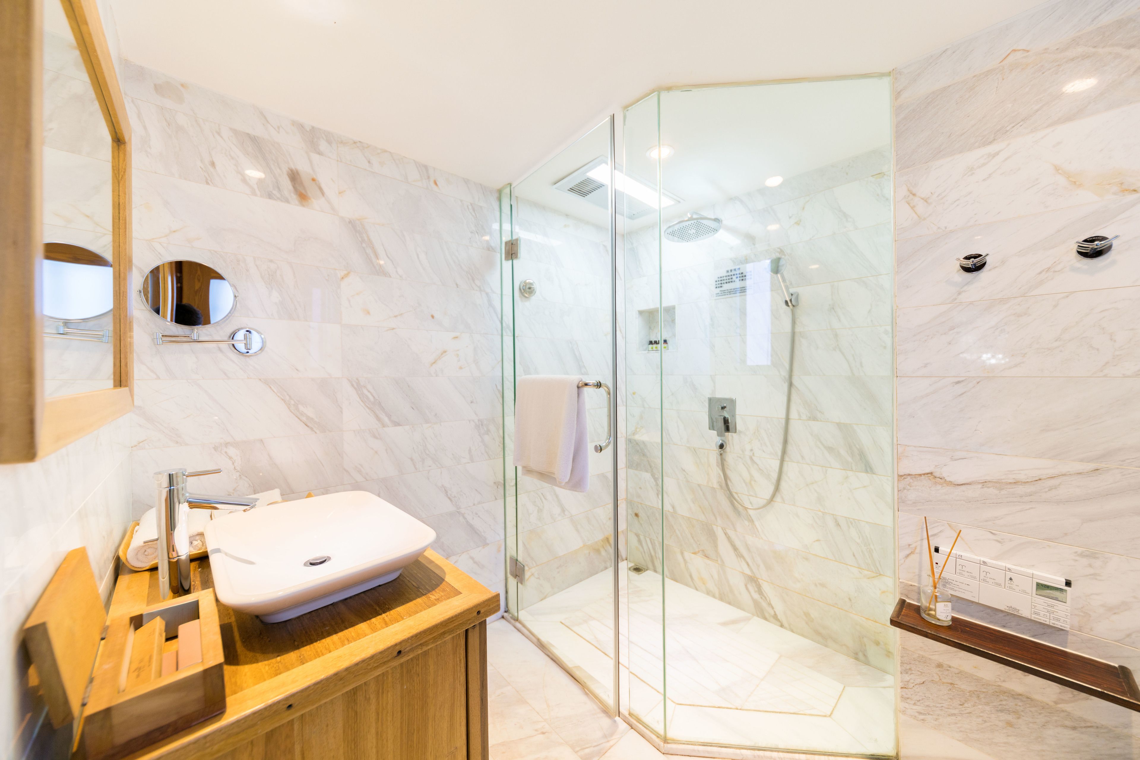 Un bagno moderno con doccia vetrata, un mobile contenitore in legno e pareti in marmo.