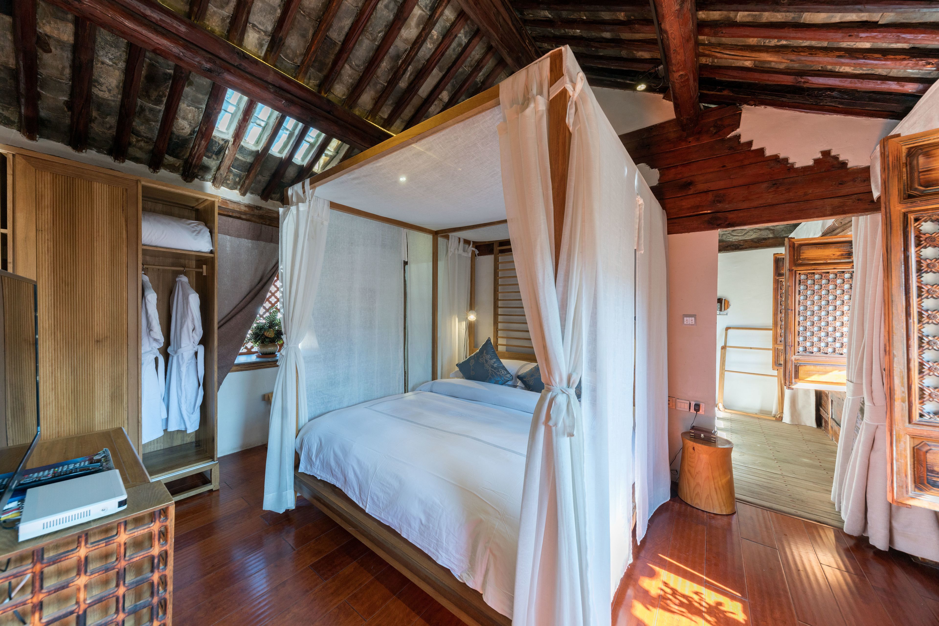 A bedroom with a canopy bed, wooden flooring, a wardrobe, and a small wooden stool.