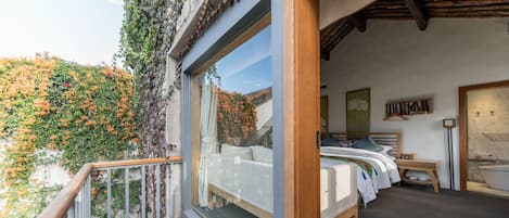 A bedroom with a large window, a wooden bed, a bedside table, and a view of a garden.