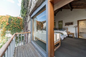 A bedroom with a large window, a wooden bed, a bedside table, and a view of a garden.