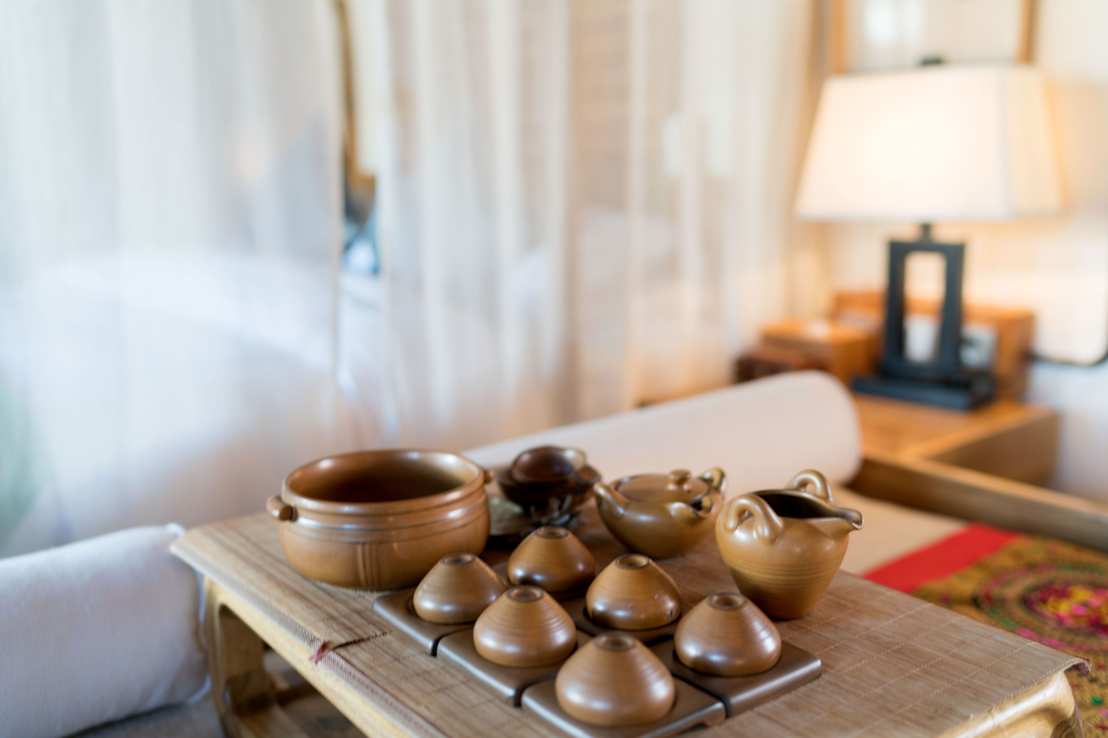 Een tafel met diverse keramieken theeserviezen en een lamp op een nachtkastje in een hotelkamer.