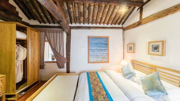 A bedroom with a wooden ceiling, a bed with a colorful embroidered bedspread, a wooden wardrobe, and a window with curtains.
