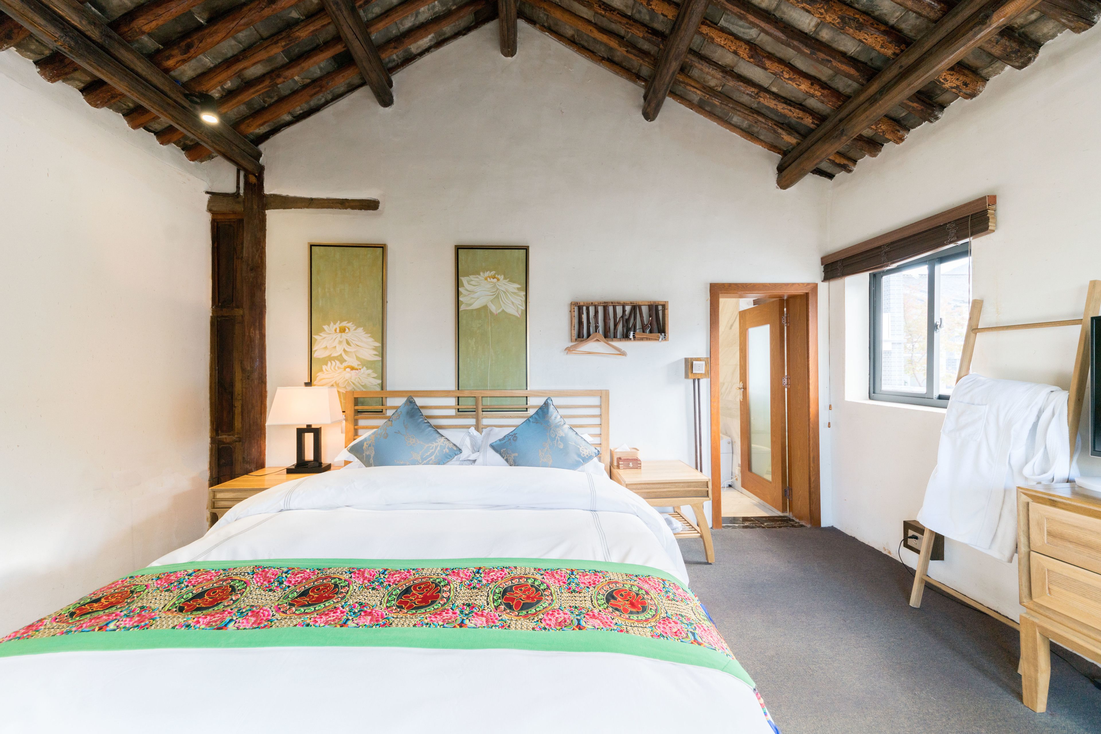 Un dormitorio con techo de madera, una cama con cubrecama floral, una mesita de noche con lámpara y un aparador de madera.