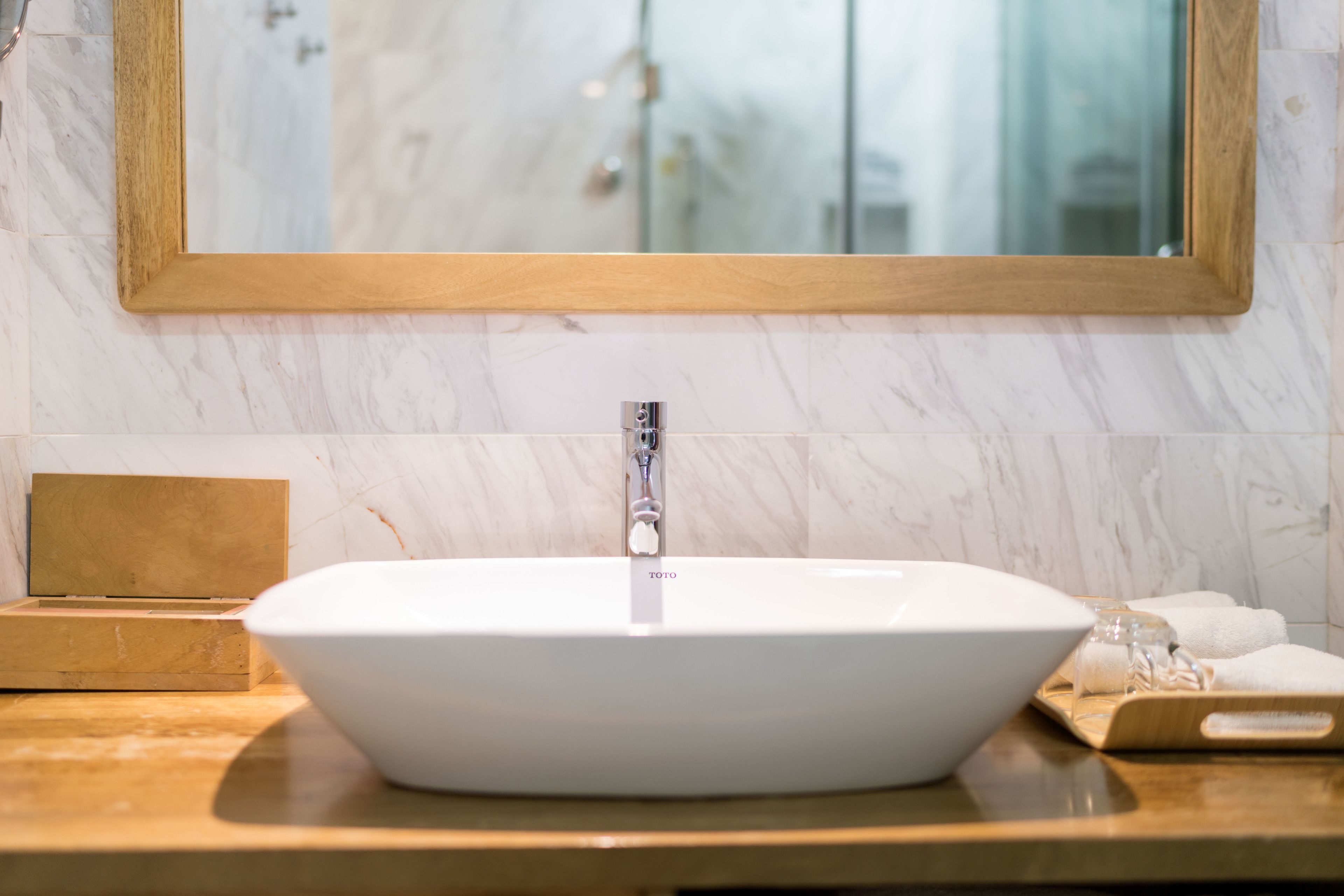 Un baño con lavamanos blanco, tocador de madera y espejo con marco de madera.