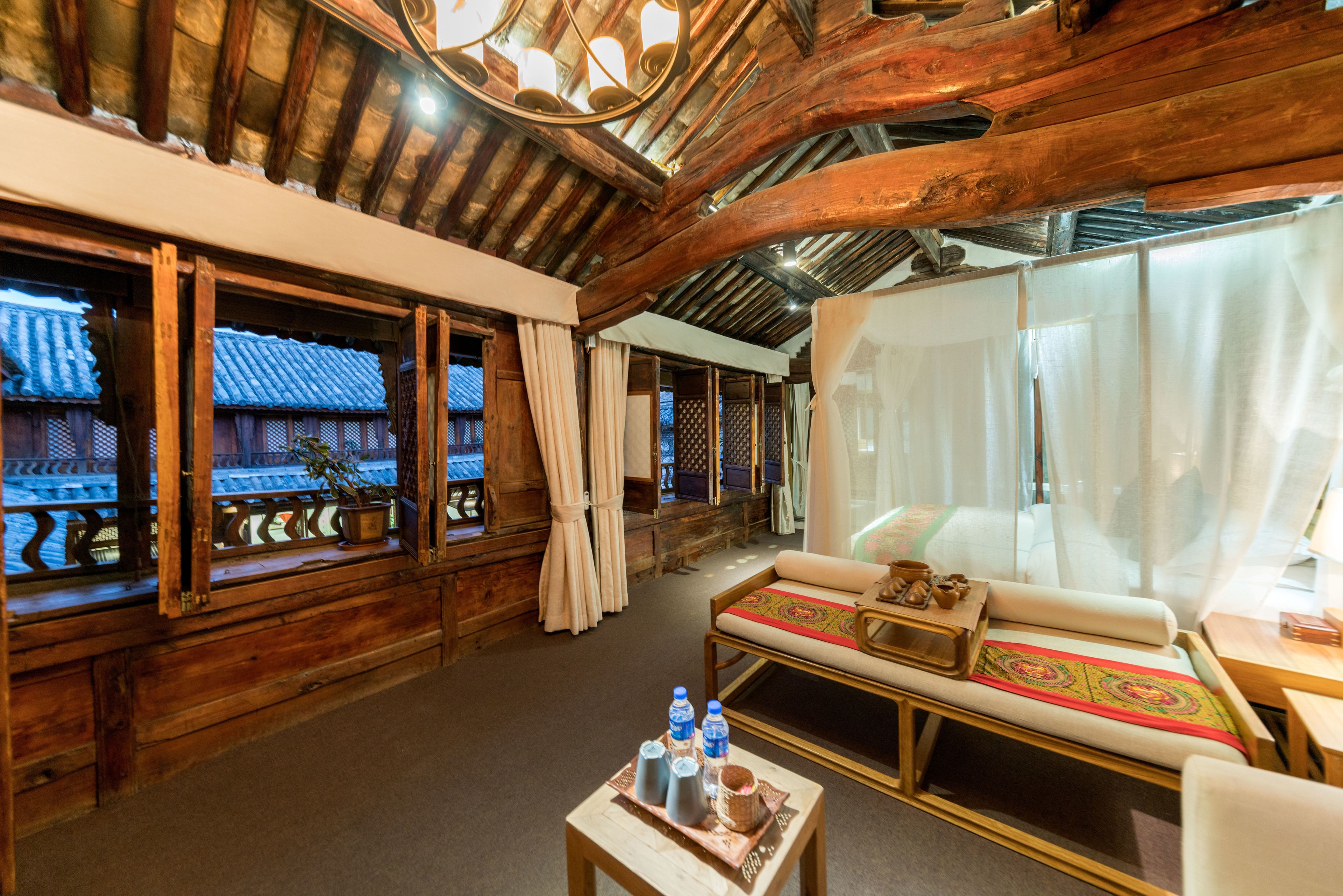 A traditional wooden interior with a sofa, a small table with bottles, and a view of a traditional building outside.