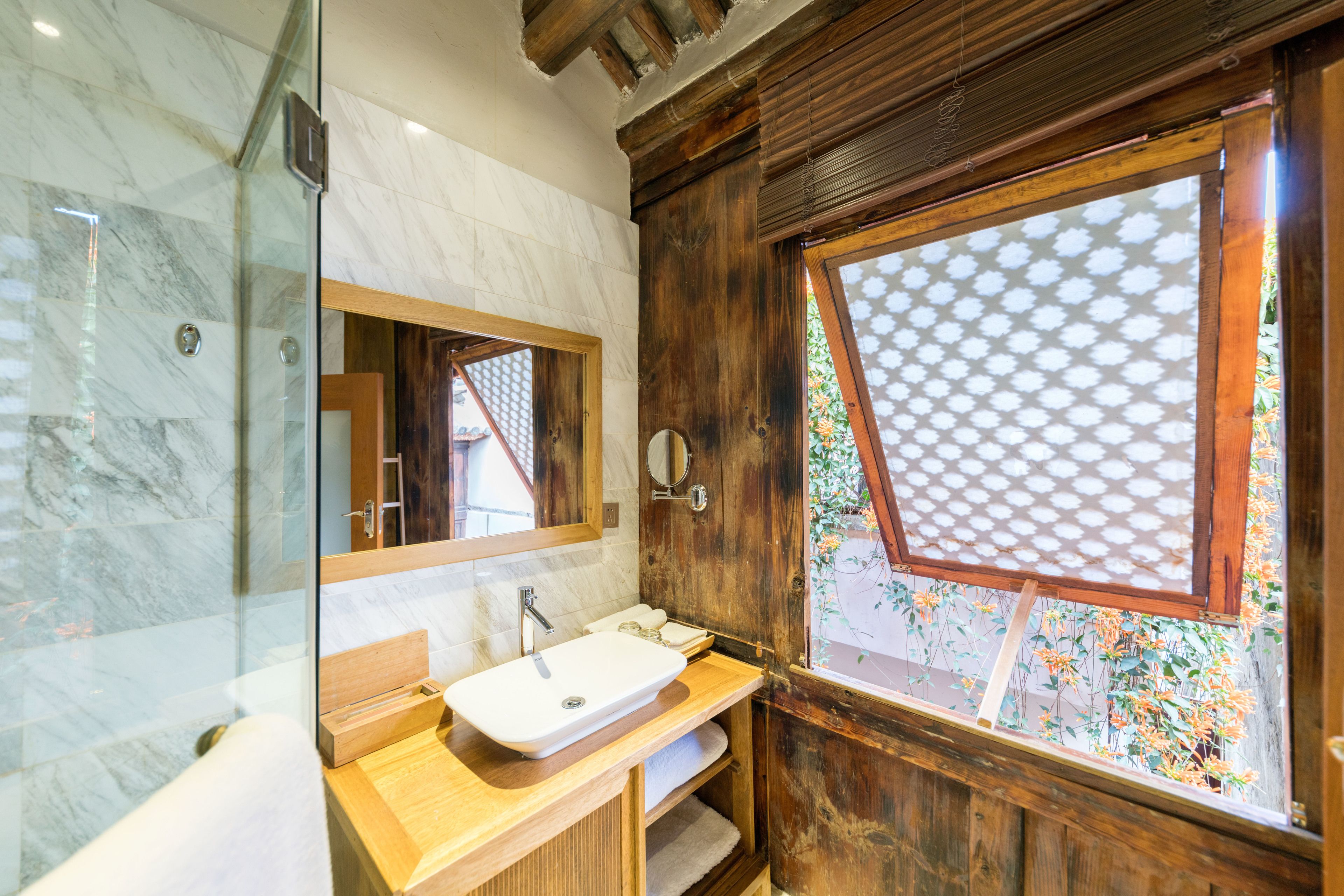 Une salle de bain avec un meuble-lavabo en bois, un lavabo blanc, un miroir et une fenêtre ornée d’un motif en croisillons.