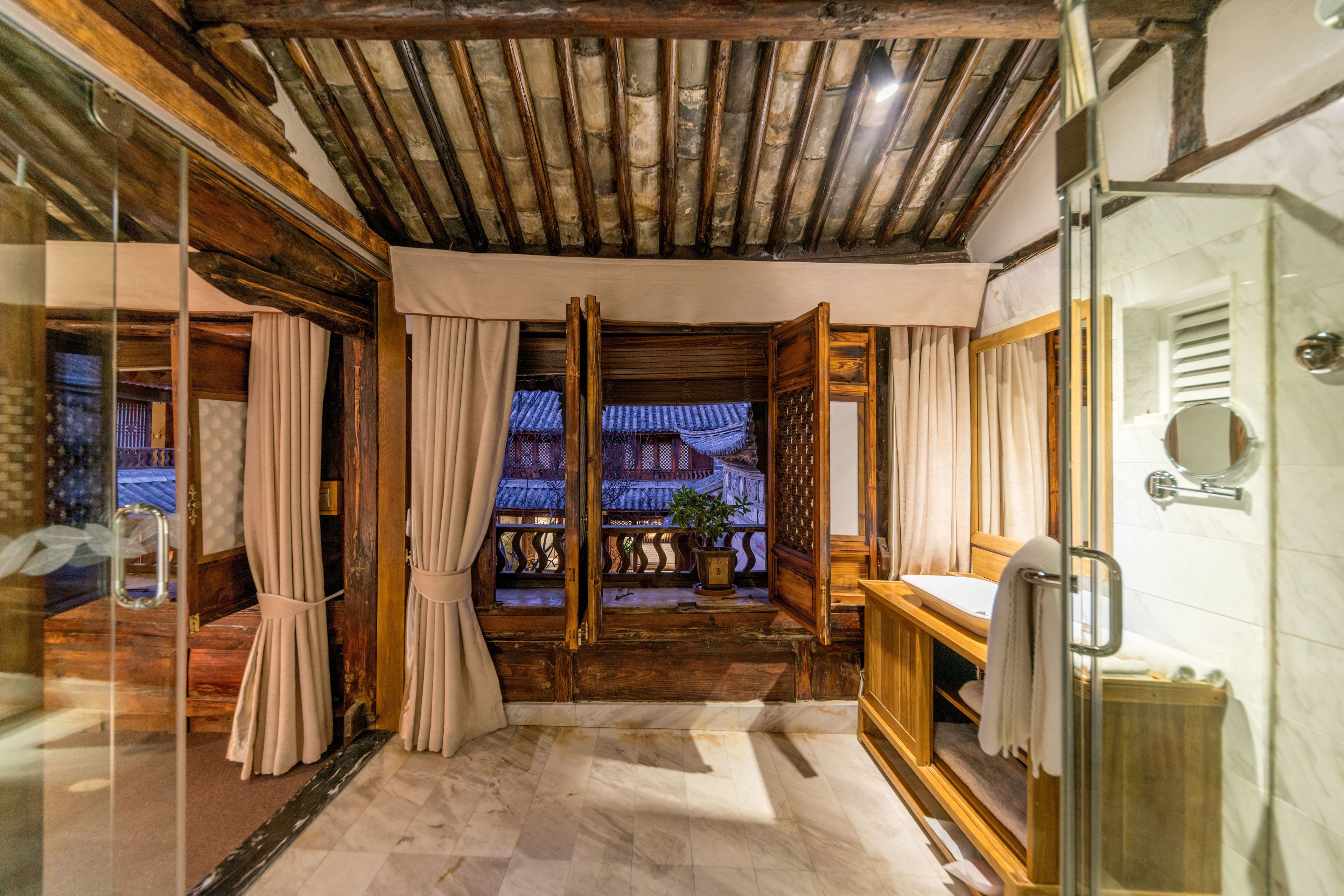 A traditional Japanese-style bathroom with a wooden ceiling, a glass shower enclosure, and a view of a traditional building outside.