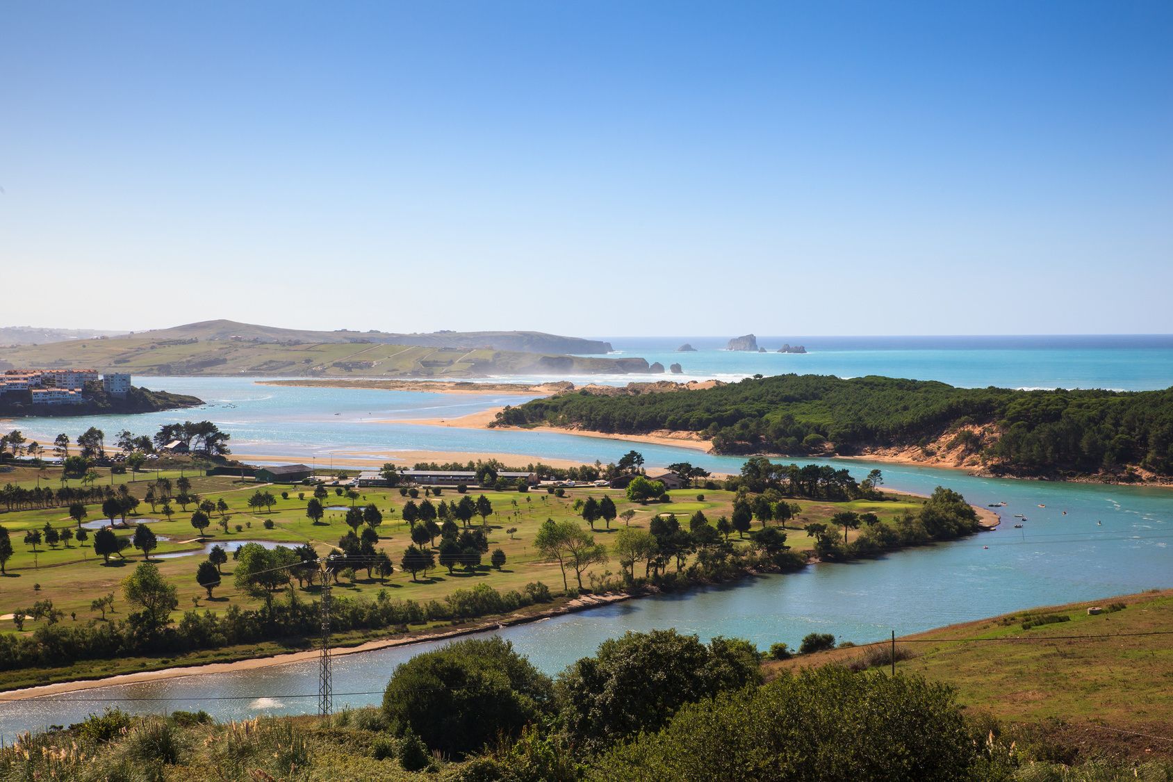 A coastal landscape with a river, green fields, and a beach.