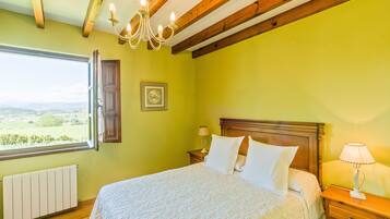 A bedroom with a bed, a nightstand, a lamp, a window with a view, and a chandelier.