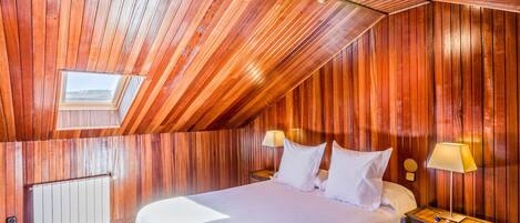 A wooden-paneled room with a bed, two bedside lamps, a window, and a radiator.