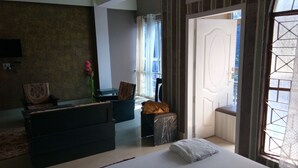 A bedroom with a large bed, a small seating area, a vanity, and a view of the outside. - Hotel Siddarth Palace (Mangaldai)