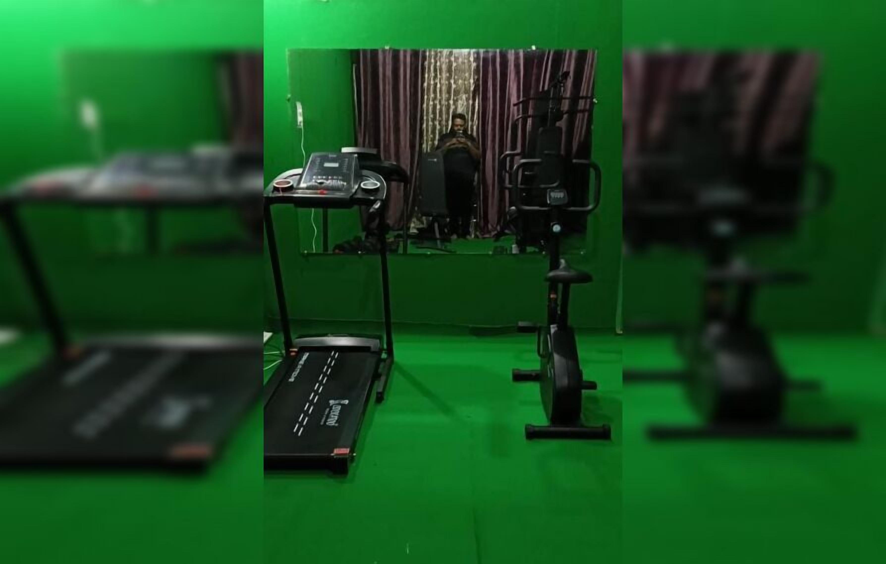 Estudio con pantalla verde, una laptop, una cinta de correr y una cámara sobre un trípode.