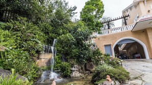 A garden with a waterfall, a stone pathway, and a building with an arched entrance. - Dragon Dalat Villa (Xuan Huong - Da Lat)
