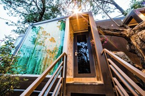A modern building with a glass facade reflecting trees, wooden stairs, and a door with a metal handle. - Dragon Dalat Villa (Da Lat)
