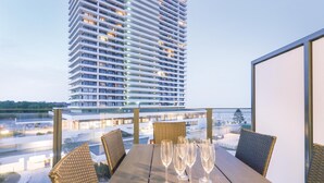 A balcony with a table set for a meal, overlooking a tall building and a cityscape. - HighEnd Travemünde - Whg 413 (Lübeck Travemünde)