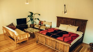 A wooden bed with a red and black blanket, a wooden chair, a television, and a potted plant in a room with wooden flooring. - Orrs (Chatan)