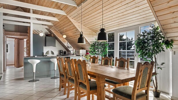 A spacious dining area with a wooden table and chairs, a kitchen in the background, and large windows allowing natural light. - Lovely home in Ringkøbing with WiFi (Ringkøbing)