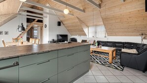 A spacious loft with a high ceiling, wooden beams, a kitchen area with a large island, a black leather sofa, and a dining table. - Lovely home in Ringkøbing with WiFi (Ringkøbing)