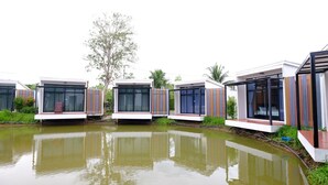 Une rangée de bâtiments modernes à un seul étage, dotés de grandes fenêtres, situés au bord d’une étendue d’eau.