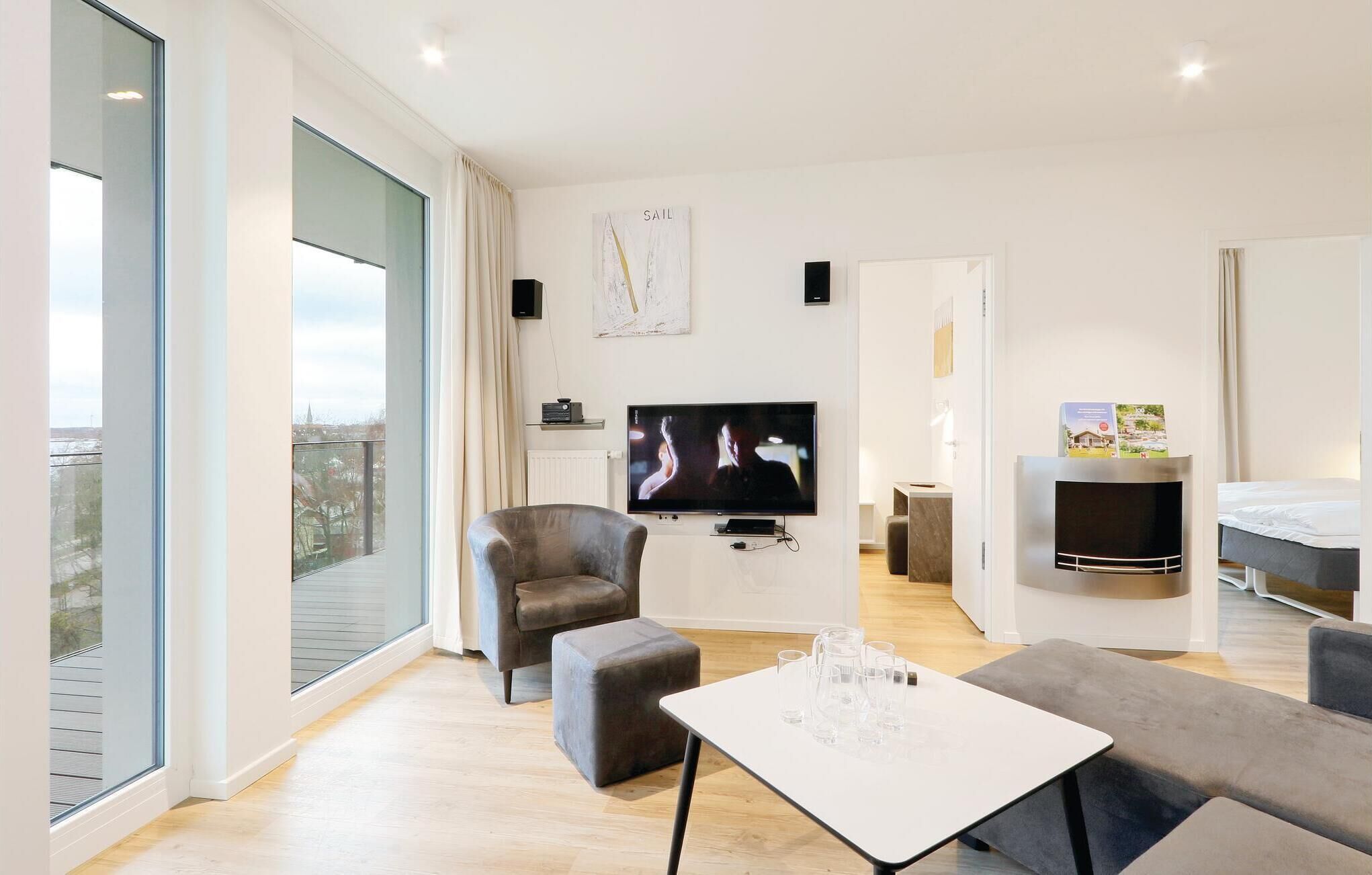 A modern living room with a large TV, comfortable seating, and a balcony with a city view.