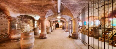 A historic underground passage with stone arches, wooden barrels, and metal railings.
