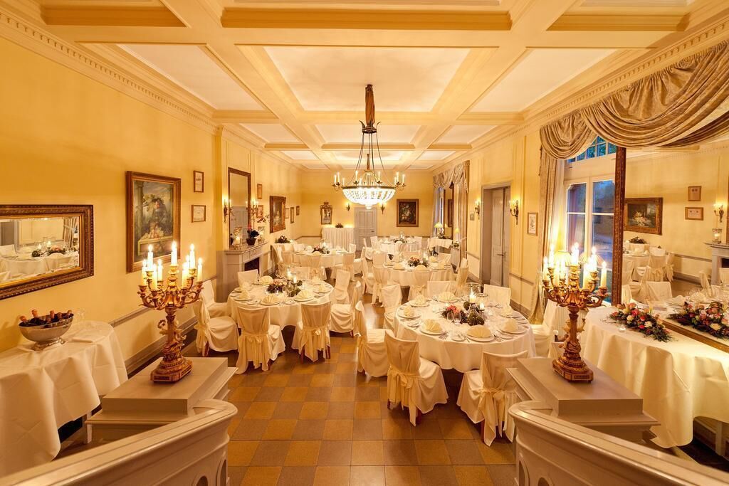 Un salón de banquetes con varias mesas redondas dispuestas para comer, candelabros y cuadros en las paredes.
