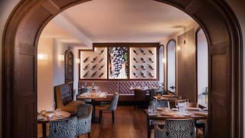 Ein Restaurant mit Holzbögen, einer zentralen Sitzgelegenheit mit gepolsterten Sitzecken und einem an der Wand befestigten Weinkühler.