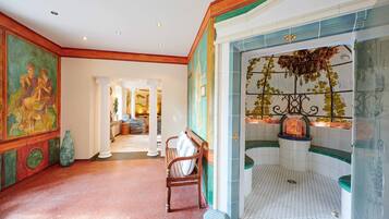 A spacious hallway with a bench, a tiled shower area with a decorative plant, and a mural on the wall.