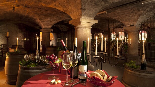 Une cave voûtée, faiblement éclairée, avec une table dressée pour le dîner, agrémentée de bouteilles de vin, de verres et de bougies.