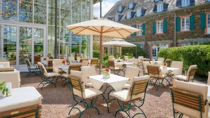 Une terrasse extérieure avec des tables et des chaises, de grandes fenêtres et un bâtiment doté d’une façade en pierre.