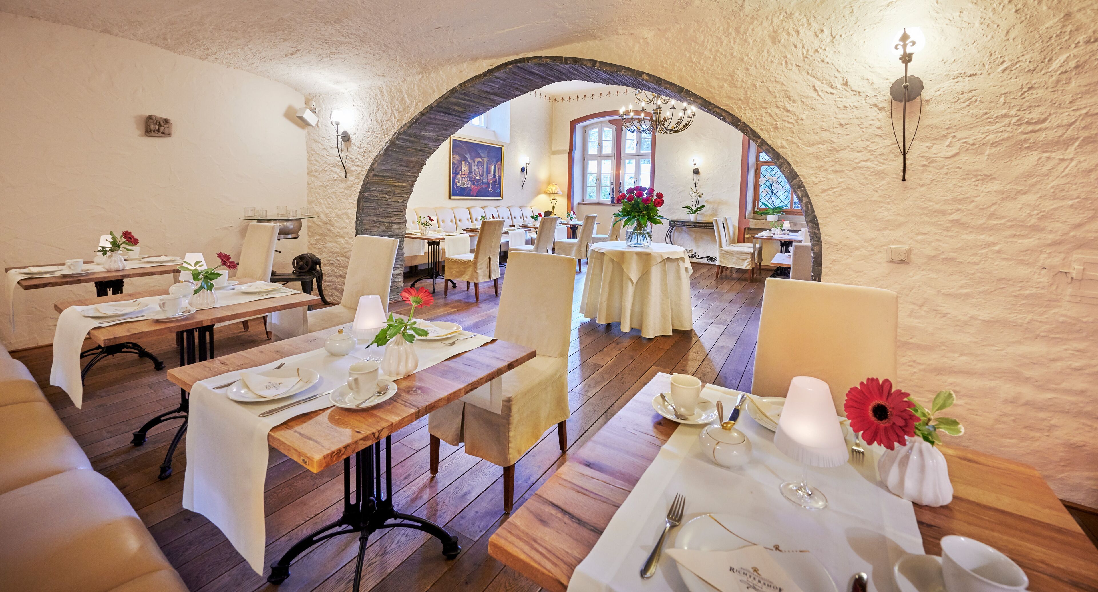Un restaurant avec des tables et des chaises en bois, des nappes blanches et des centres de table floraux.