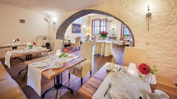 Un restaurant avec des tables et des chaises en bois, des nappes blanches et des centres de table floraux.