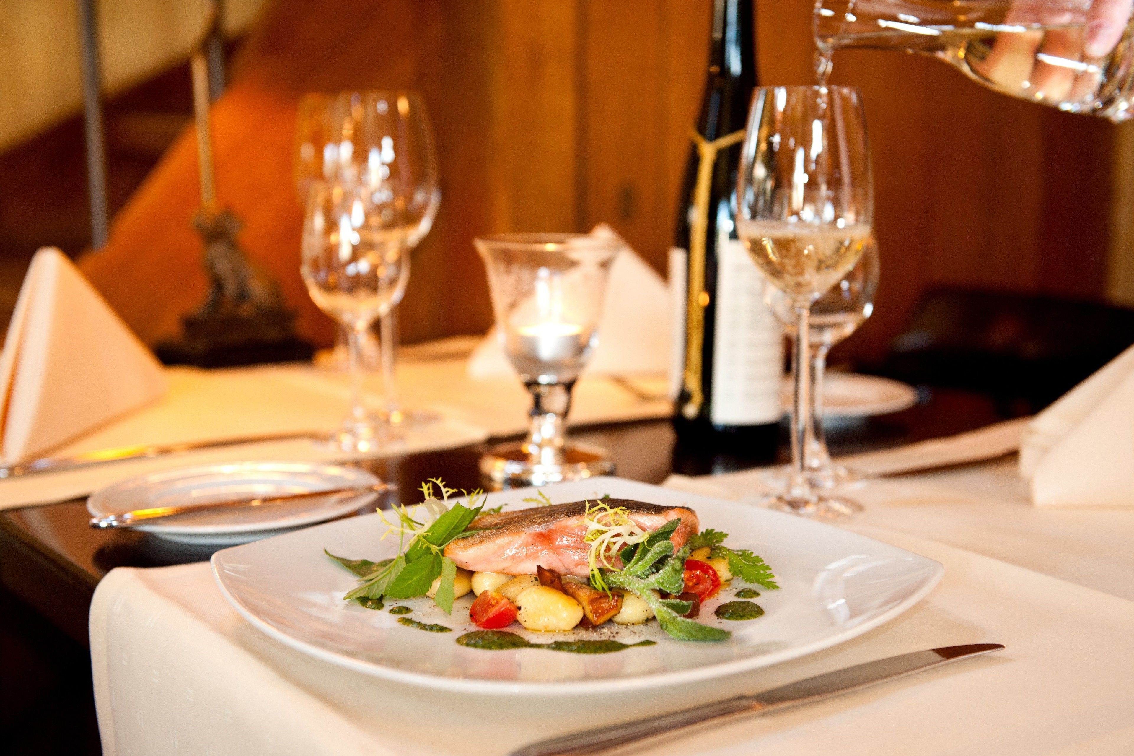 A dining table with a plate of food, wine glasses, and a bottle of wine.
