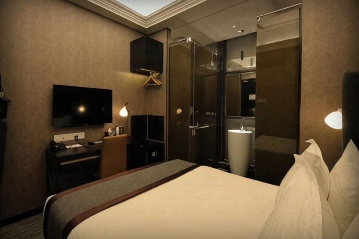 A hotel room with a bed, a desk, a television, a mirror, and a bathroom.