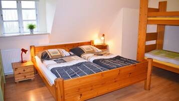 Uma cama beliche de madeira com uma mesa de cabeceira e abajur, uma janela com uma planta, e um radiador.