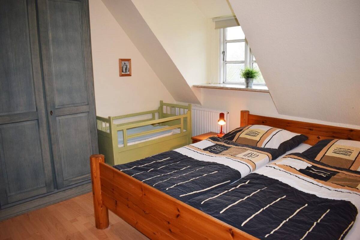 Une chambre avec un lit en bois, une fenêtre donnant sur un beau paysage et un radiateur.