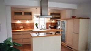 A modern kitchen with wooden cabinets, a central island, and a built-in oven. - Reetdachhaus Bongsiel (Ockholm)