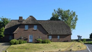 A traditional brick building with a thatched roof, a small porch, and a signboard. - Reetdachhaus Bongsiel (Ockholm)