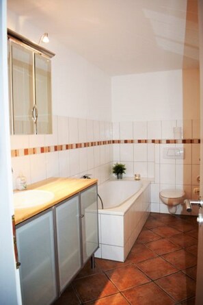 Een badkamer met een houten wastafelmeubel, een badkuip en een toilet.