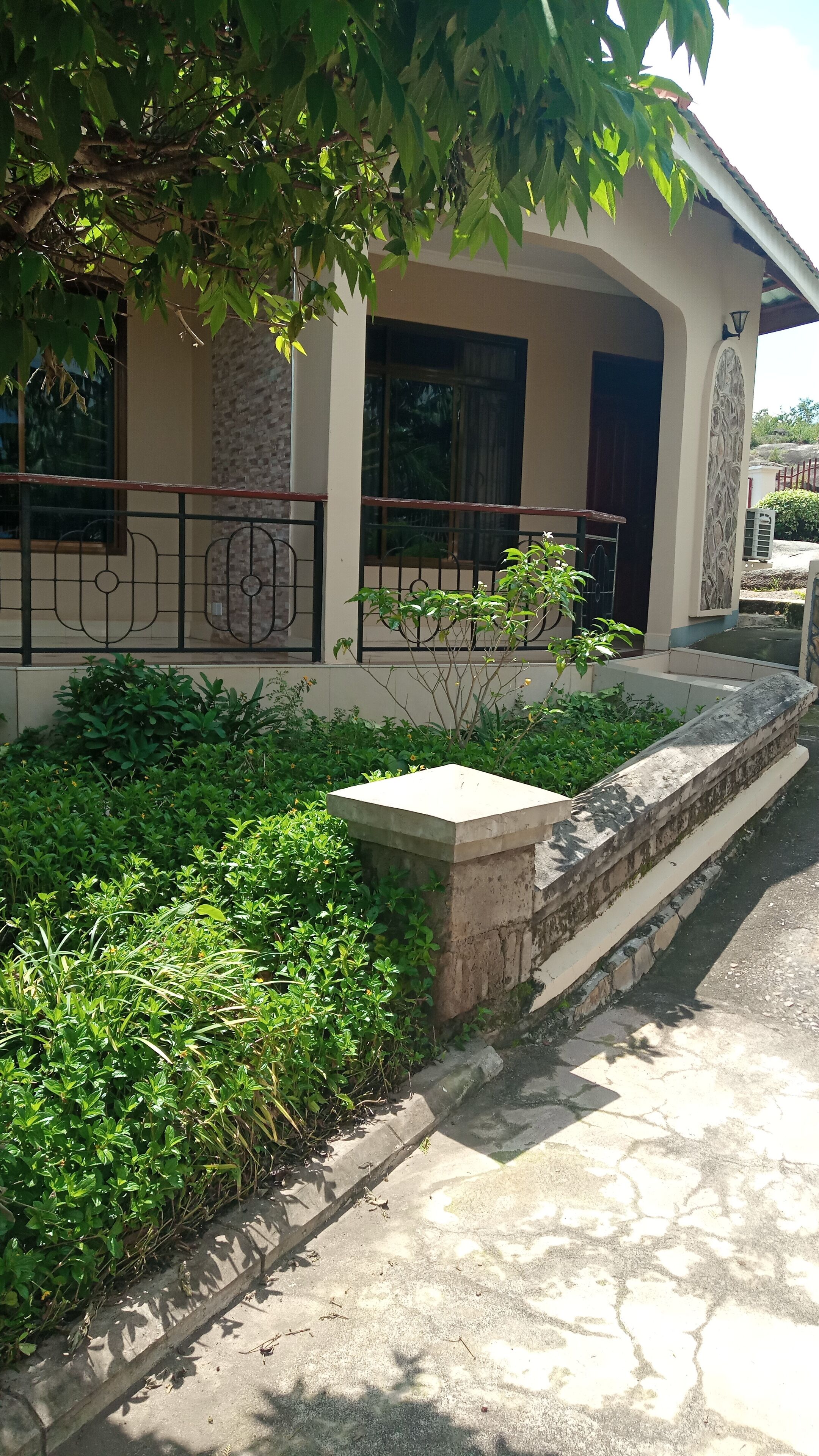 Una casa con balcón, pared de piedra y jardín con diversas plantas.