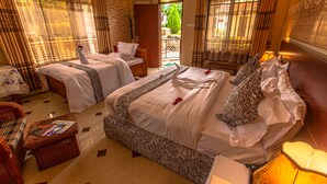A hotel room with two beds, a sitting area with a wicker chair, and a view of the garden through the door.