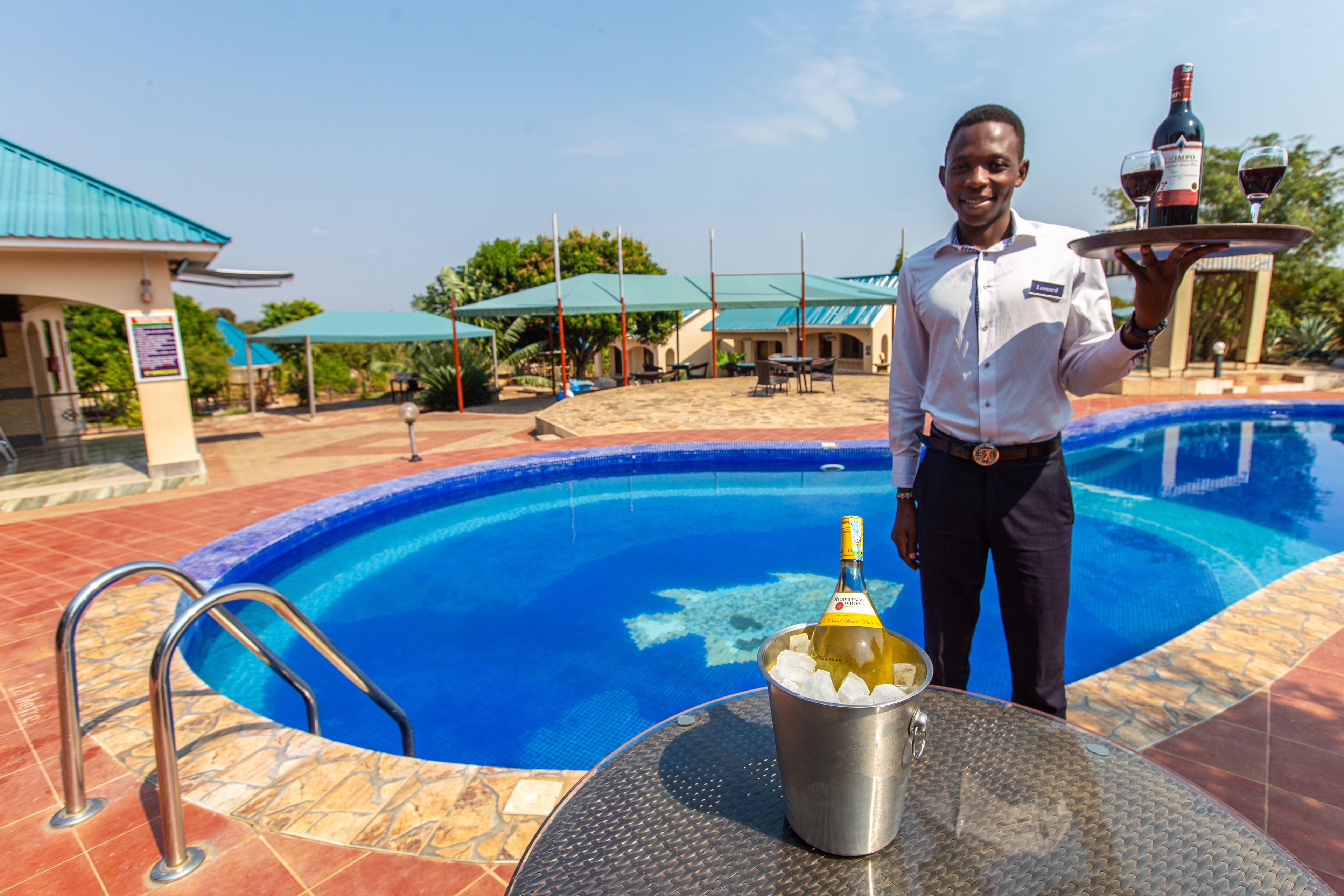 A poolside area with a lifeguard stand, a table with a bottle of champagne, and a tray with glasses and a bottle.