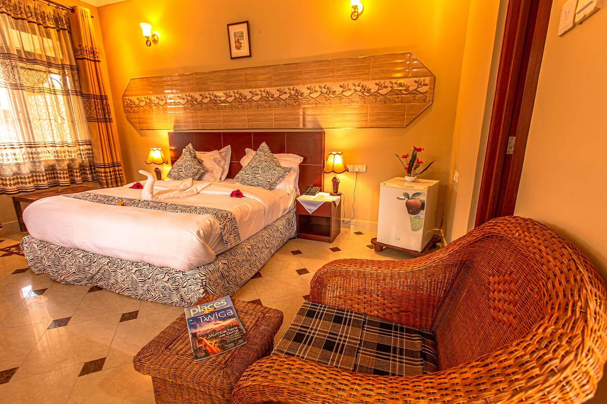 Quarto de hotel com uma cama grande, um sofá, uma mesinha e uma mesa de cabeceira com luminárias.