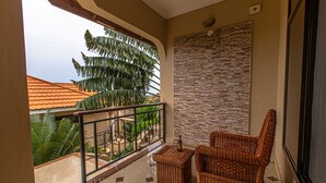 A balcony with a wicker chair, a small table, and a view of a palm tree and buildings.