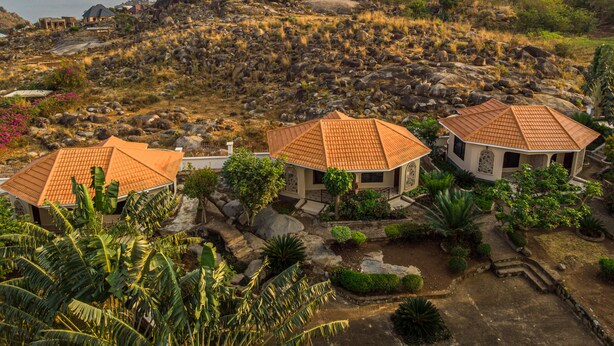 A hillside property with three buildings featuring terracotta roofs, surrounded by lush vegetation and rocky terrain.
