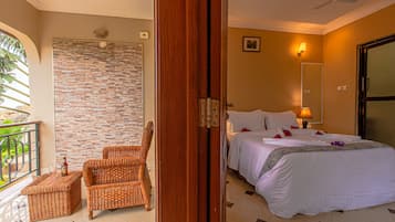 Habitación de hotel con cama, una silla, una mesita pequeña, balcón y pared de ladrillo.