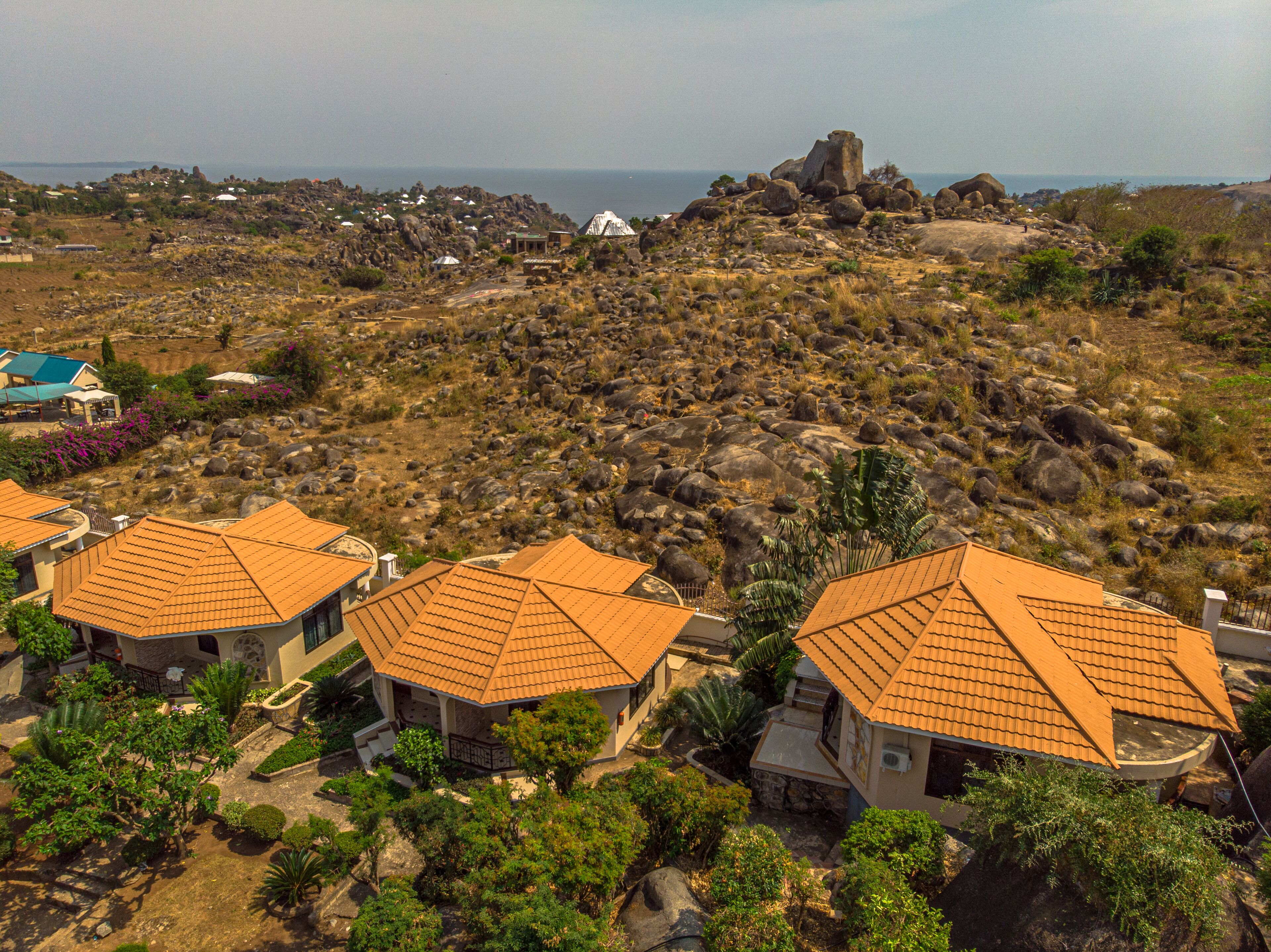 A residential area with houses featuring orange-tiled roofs, surrounded by rocky terrain and sparse vegetation.