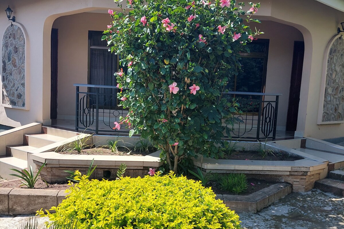 Ein Haus mit Ziegeldach, einem Balkon und einem Garten mit rosa Blumen und grünen Sträuchern.