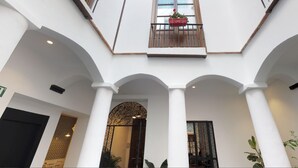 A spacious atrium with white columns, a central archway, and a balcony with a potted plant. - Madeinterranea Suites (Málaga)