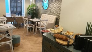 A dining area with wicker chairs, a white table, and a buffet with various food items. - Madeinterranea Suites (Málaga)